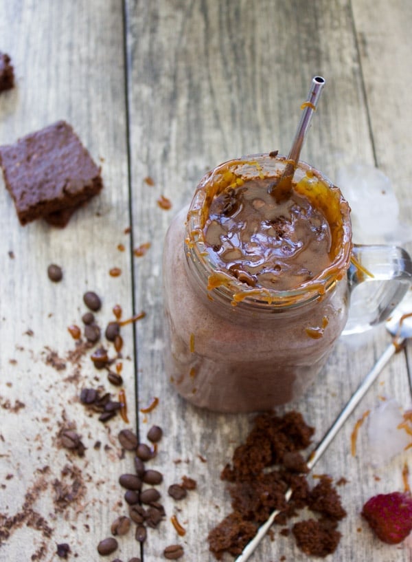 caramel-drizzled Espresso Brownie Chocolate Smoothie served in a mason jar glass with a straw and some crumbled brownies in the background