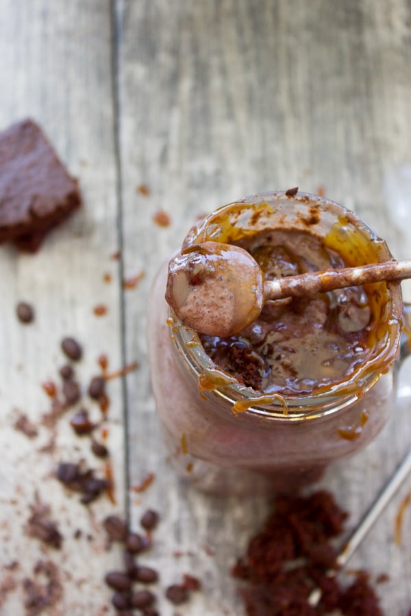 caramel-drizzled overhead shot of a small spoon being dipped into a creamy Espresso Brownie Chocolate Smoothie served in a mason jar glass