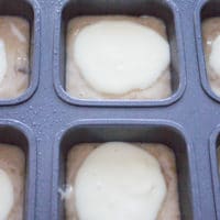 banana bread muffins batter being topped with a cream cheese layer in a muffin pan