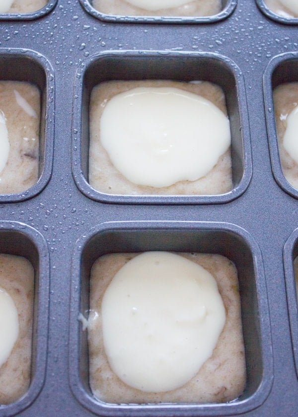 banana bread muffins batter being topped with a cream cheese layer in a muffin pan