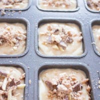 banana bread muffins batter in a muffins pan being topped with streusel topping before baking