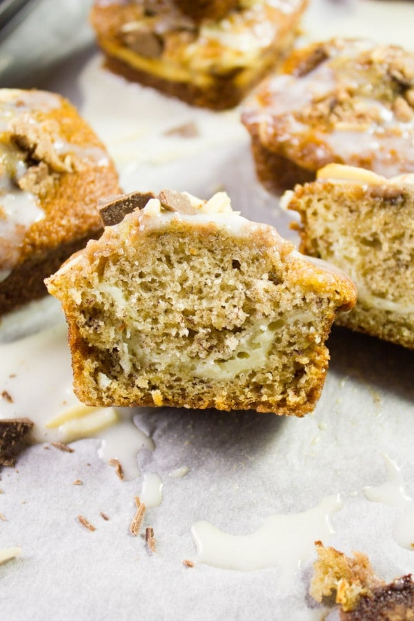 One banana bread muffin right out of the oven glazed and ready, then cut in half showing the texture and cream cheese swirl