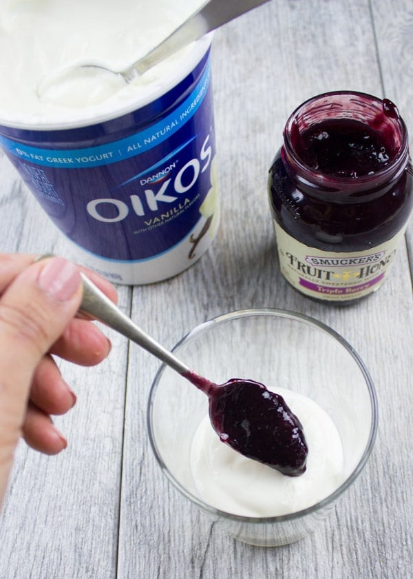 berry jam being spooned on top of vanilla yogurt in a small glass bowl