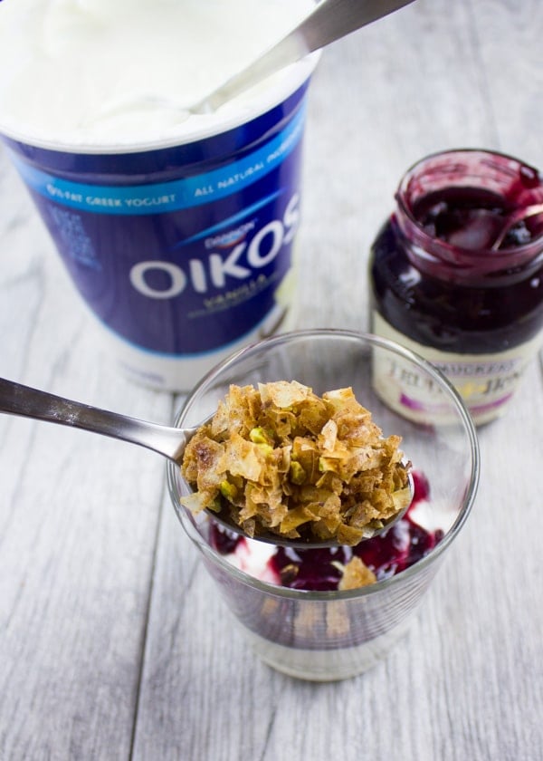 Baklava Crumble being spooned on top of a layer of vanilla yogurt and berry jam