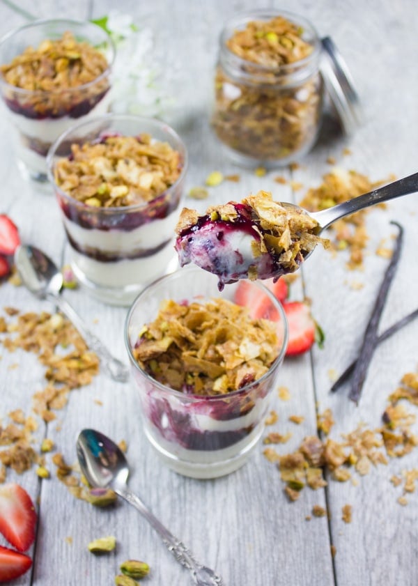 a spoon of baklava crunch-topped yogurt parfait being balanced over a glass with yogurt parfait