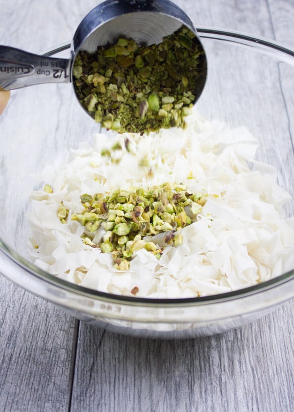 pistachios being added to a bowl with shredded phyllo dough