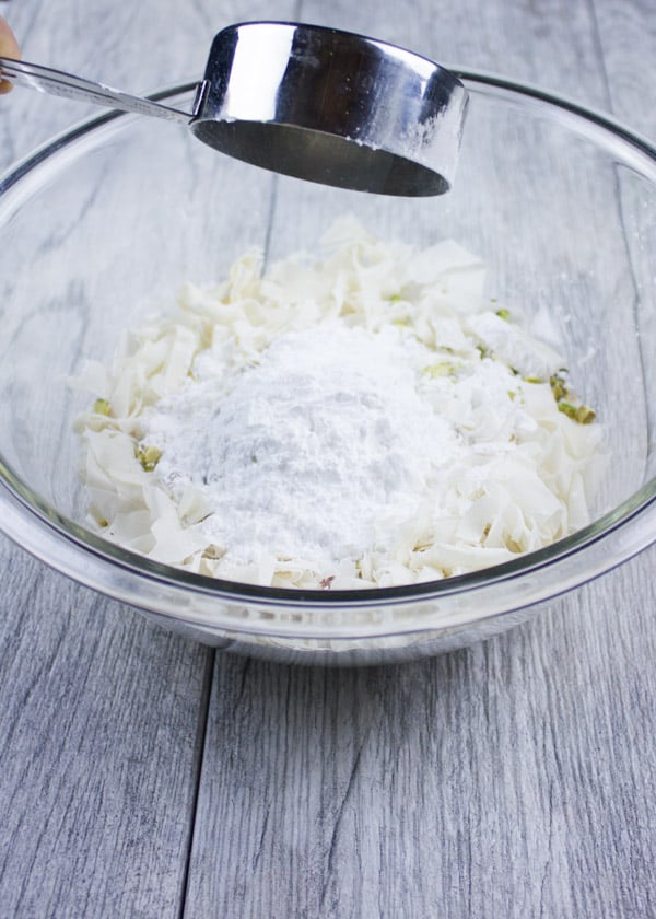 powdered sugar being added to a bowl with shredded phyllo dough