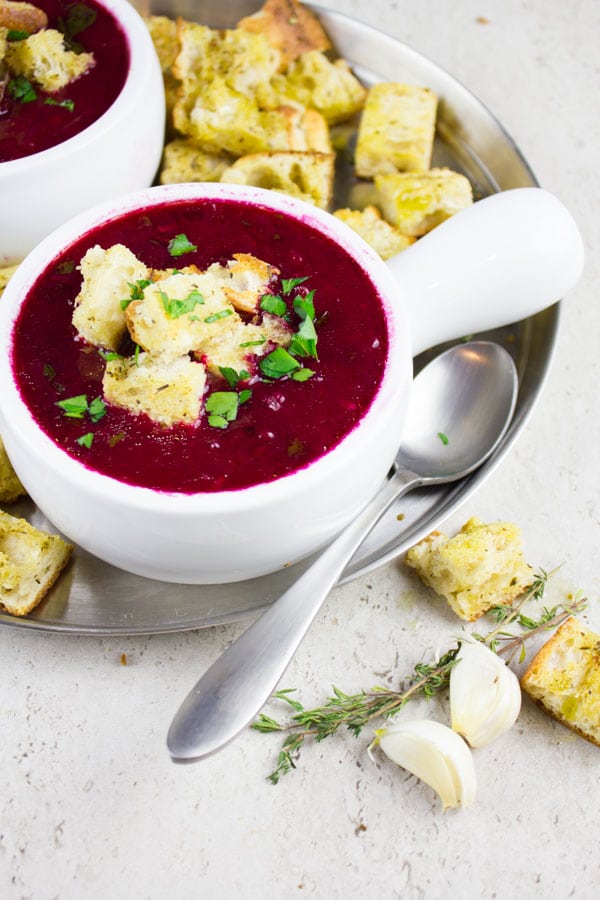side view of two small bowls of Russian beetroot soup with croutons on top and on the side