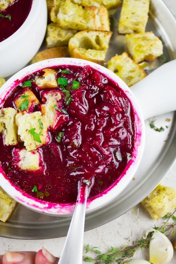 overhead shot of a bowl of Russian Beetroot Soup with croutons on top and on the side