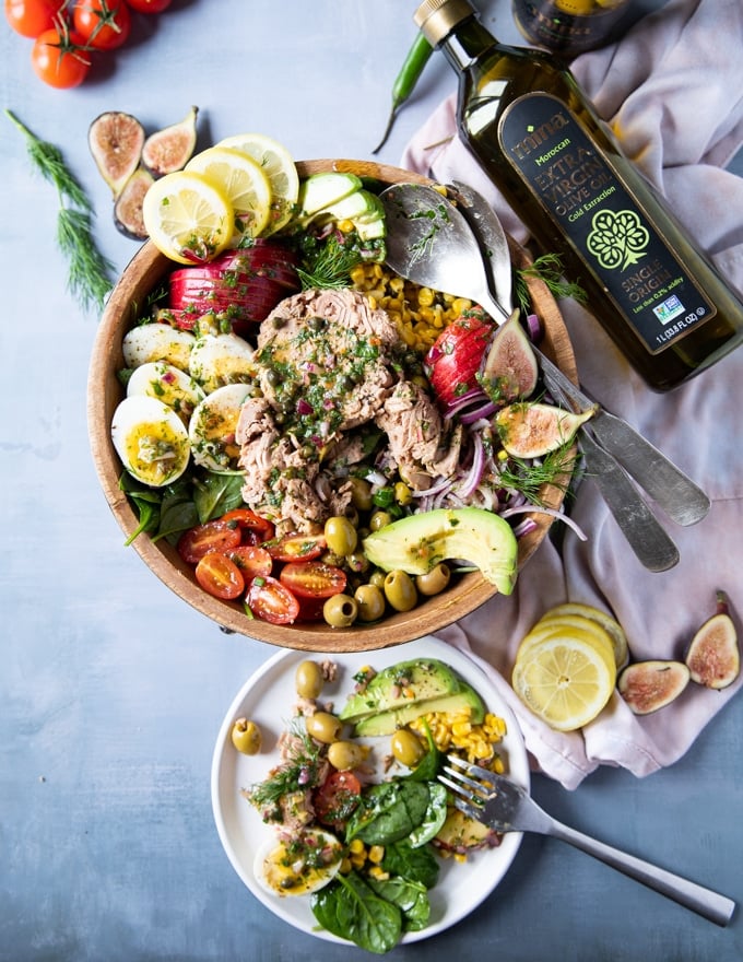 a small plate next to the tuna salad recipe served up with tuna salad. some spinach, tuna, avocado, hard boiled egg on the small plate and a fork eating them