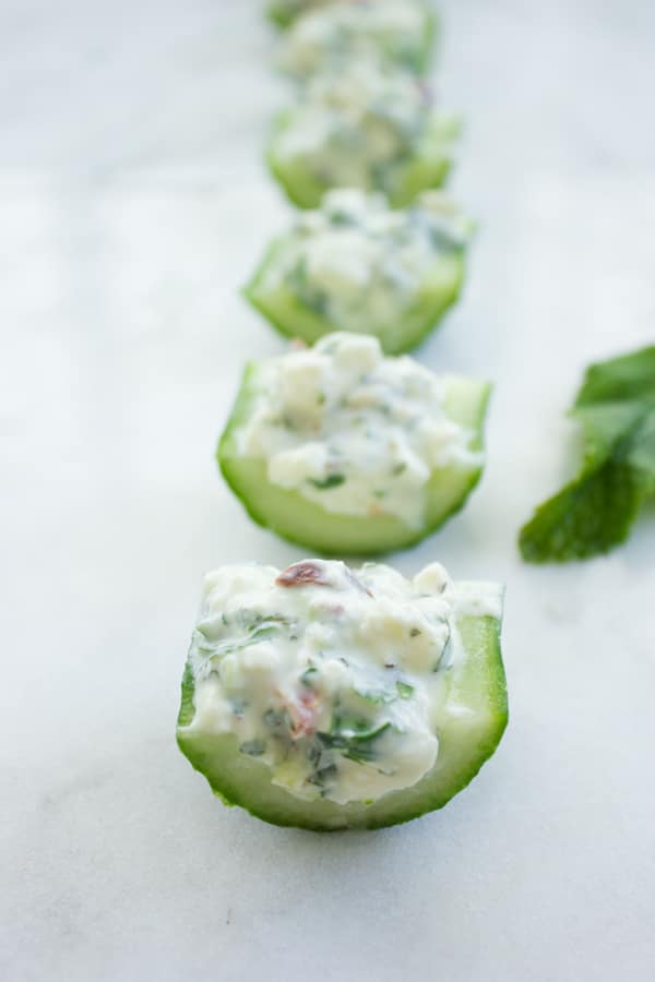 Close-up of bite-sized cucumber pieces filled with feta cream lined up in a row