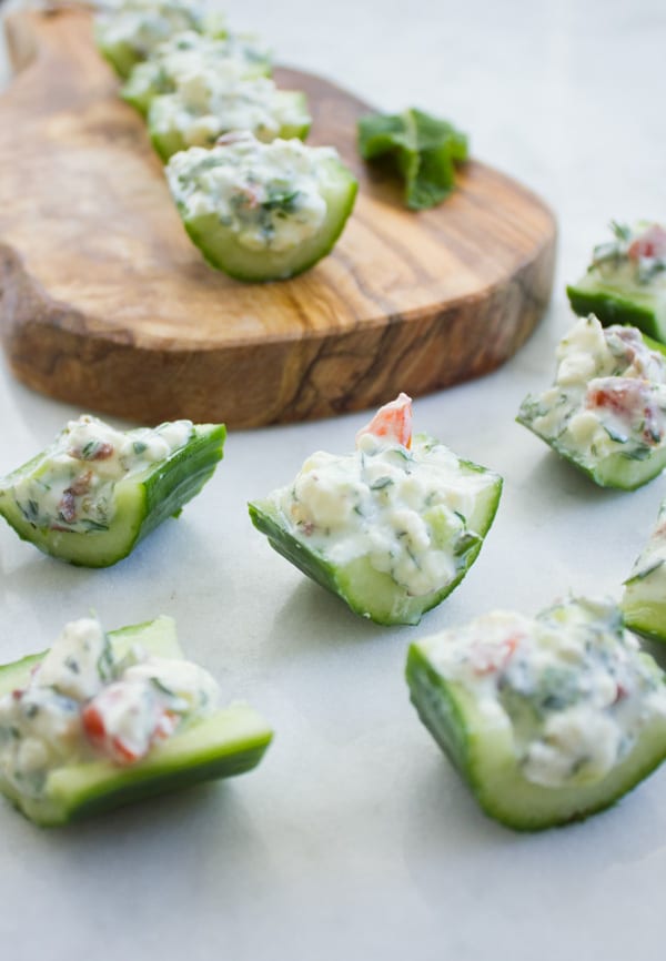 Cucumber Salad Bites filled with herbs, feta cheese and tomatoes arranged on a wooden chopping board 