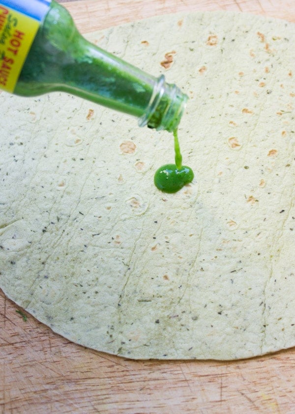 hot sauce being drizzled on top of a wheat tortilla