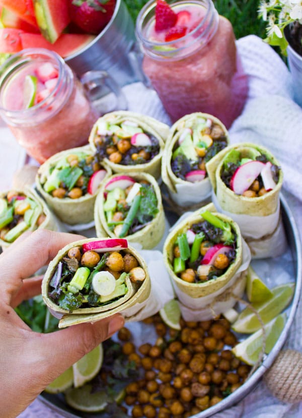 a hand holding a Roasted Chickpeas Wrap with more wraps and some cocktails in the background