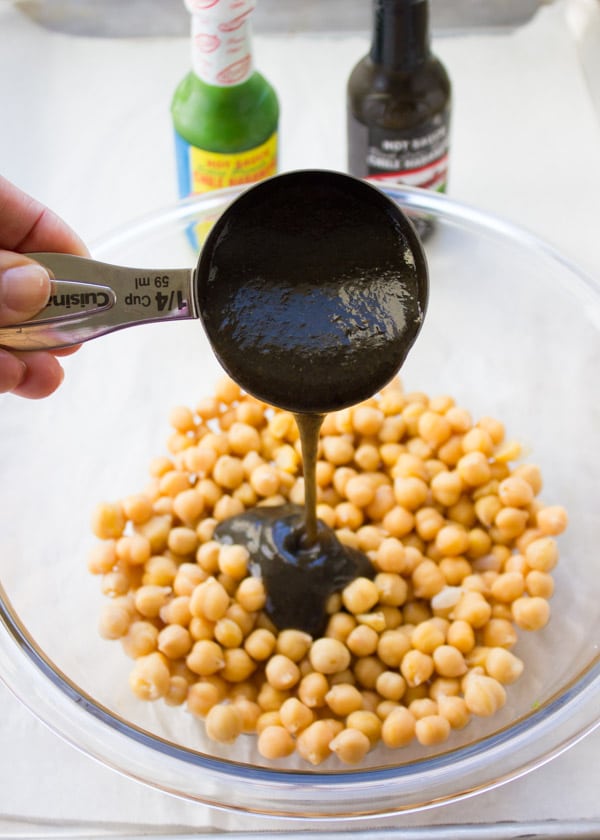 seasoning sauce being added to a bowl with canned chickpeas to make roasted chickpeas