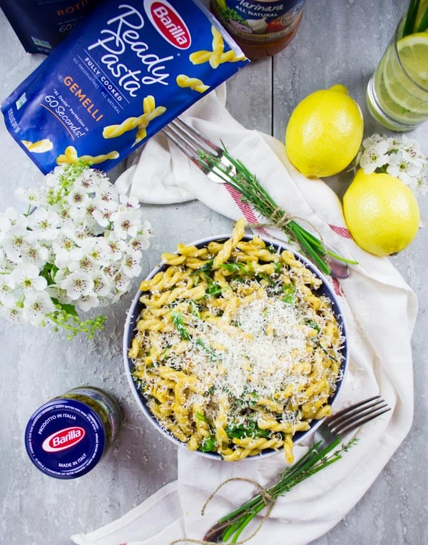 overhead shot of a bowl of lemon pasta topped with grated parmesan and lemons and herbs on the side