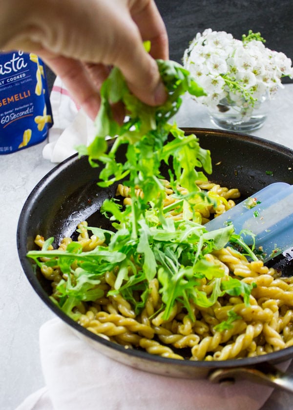 arugula being added to a skillet with pasta