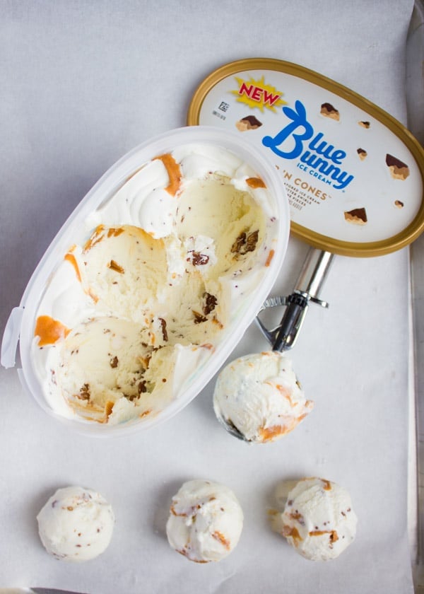 Some ice cream scooped over a parchment paper and the box of ice cream opened with the scoop.