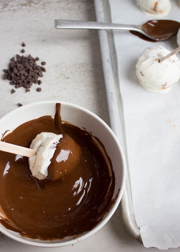 dipping the ice cream scoop with a stick in melted chocolate