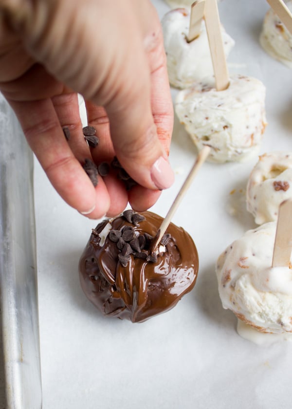 A hand sprinkling chocolate chips over melted chocolate on the ice cream pops.