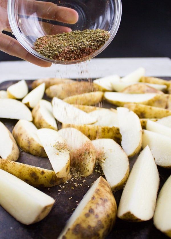 a spice mix being sprinkled on top of unbaked potato wedges