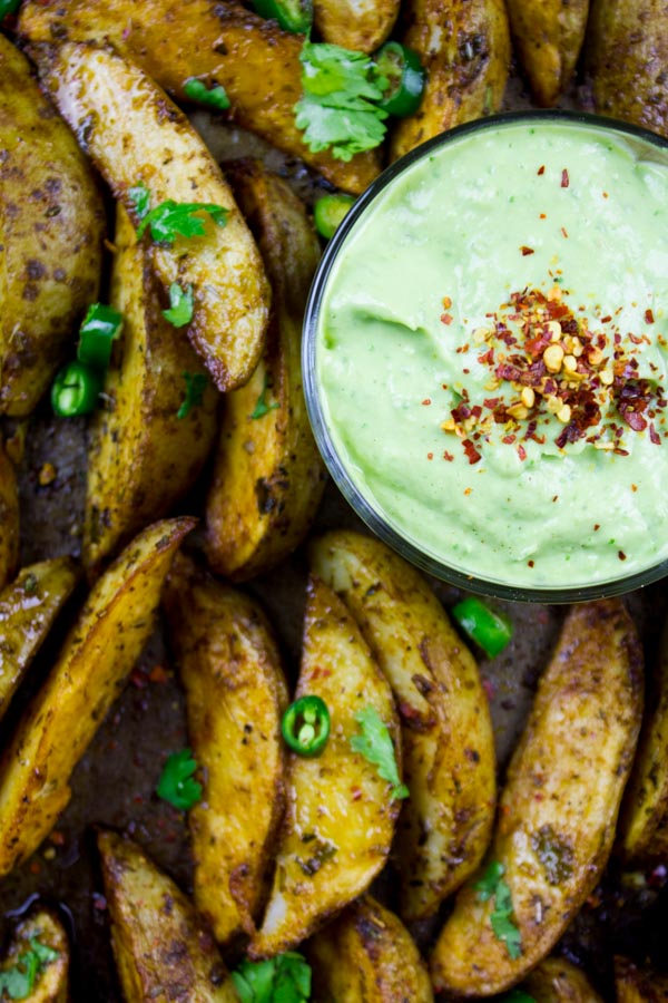 Perfect Baked Potato Wedges on a black baking tray served with Avocado Crema in a small dish