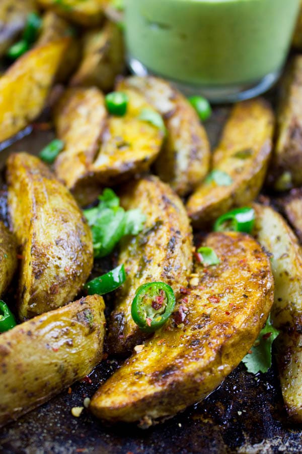 close up of Perfect Baked Potato Wedges on a black baking tray served with Avocado Crema in a small dish