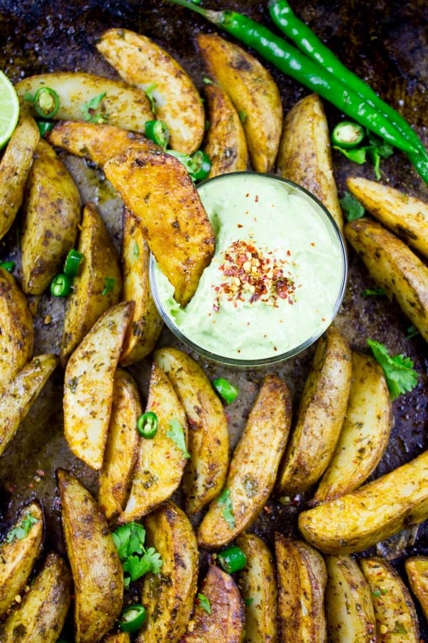 Perfect Baked Potato Wedges on a black baking tray served with Avocado Crema in a small dish