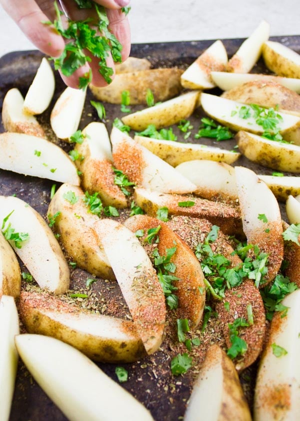 unbaked potato wedges being seasoned with Mexican spices
