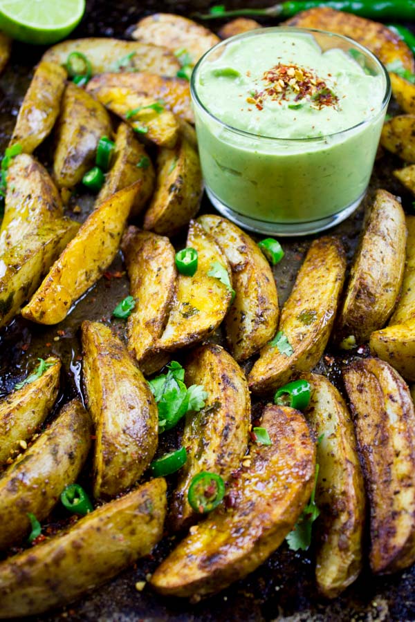 Perfect Baked Potato Wedges on a black baking tray served with Avocado Crema in a small dish