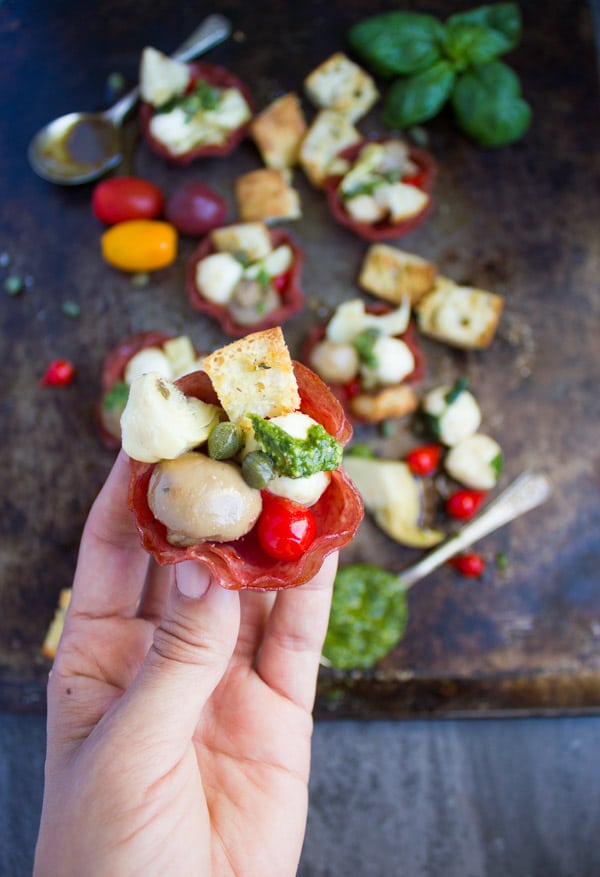 a hand holding a bite-sized salami cup filled with antipasto