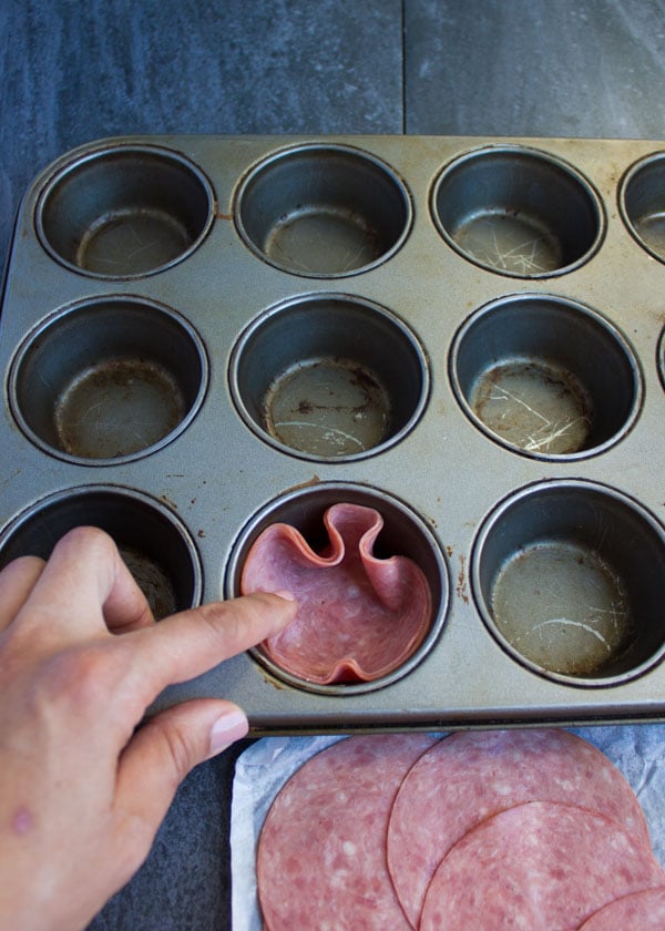 a muffin pan being lined with salami slices to make salami cups