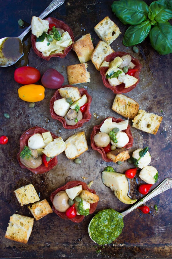 Antipasto Salami Cups and homemade bread croutons arranged on a rustic baking tray with some pesto on the side