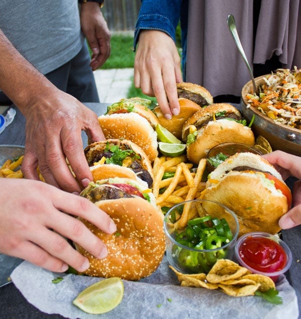 hand reaching for lamb burgers arranged on a pile of french fries with little side dishes with ketchup and guacamole nestles in between the fries.