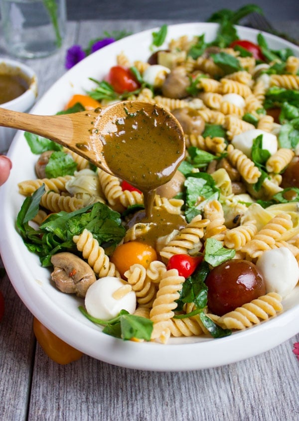 basil balsamic dressing being drizzled on top of Warm Antipasto Platter Pasta