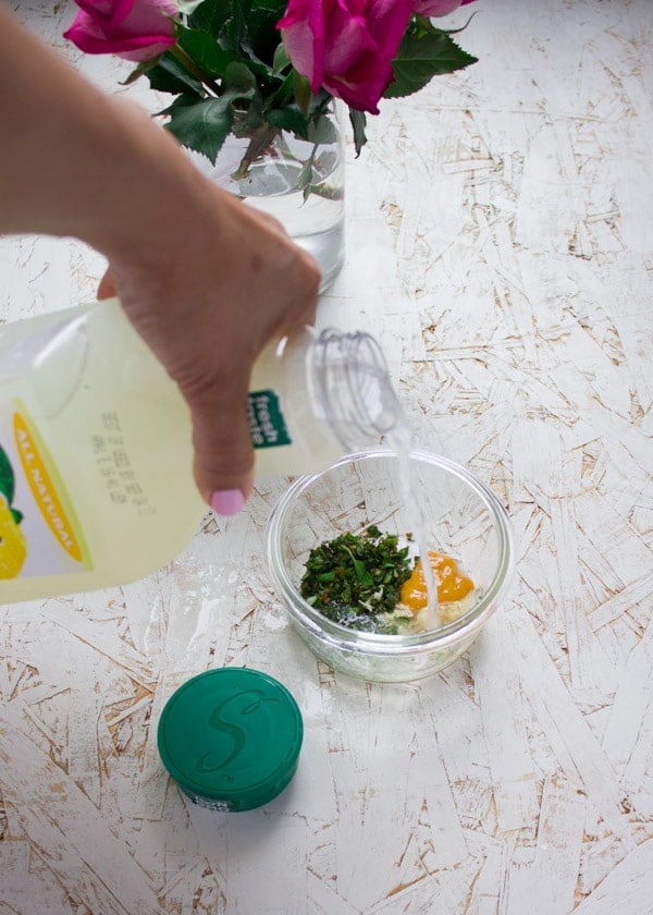 lemonade being poured into a glass bowl with spices and herbs to make a salad dressing.