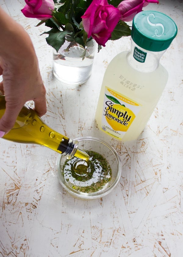 olive oil being drizzled into a glass bowl with lemonade dressing.