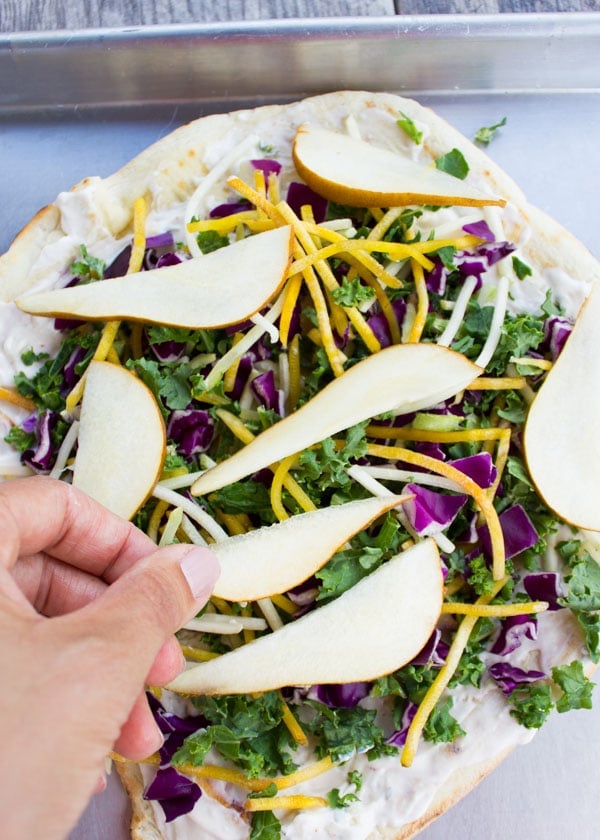 Pear Slices being put on top of a Veggie Pizza On the Grill topped with kale, golden beets and cabbage 