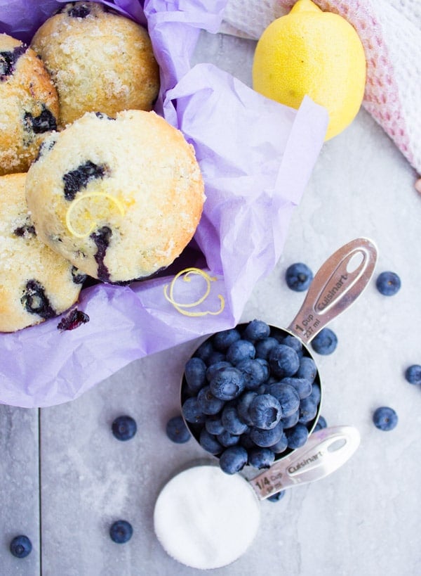 Freshly baked Blueberry Muffins topped with Lemon Sugar Crunch piled up next to a cup of blueberries