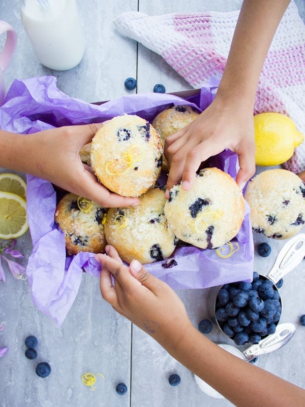 Children hands reaching for Blueberry Muffins from a box on a rustic white table