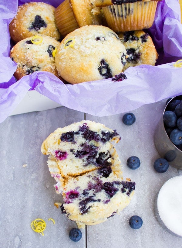 Moist Blueberry Muffin split into two halves with some fresh blueberries and muffins in the background