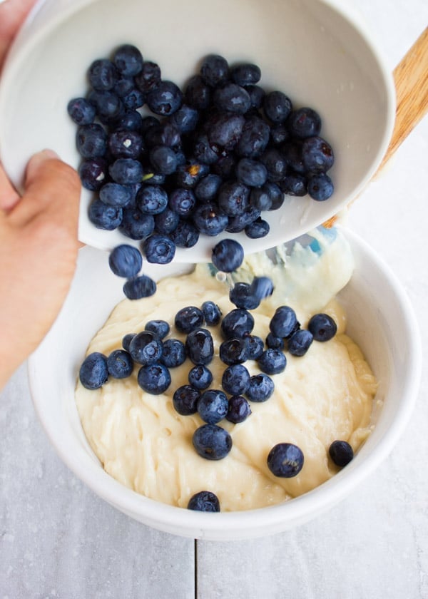 fresh blueberries being added to a bowl with muffin batter 