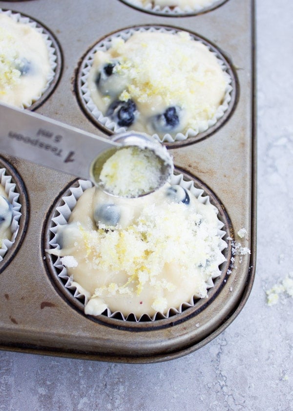 Lemon Sugar Crunch topping being sprinkled onto unbaked Blueberry Muffins