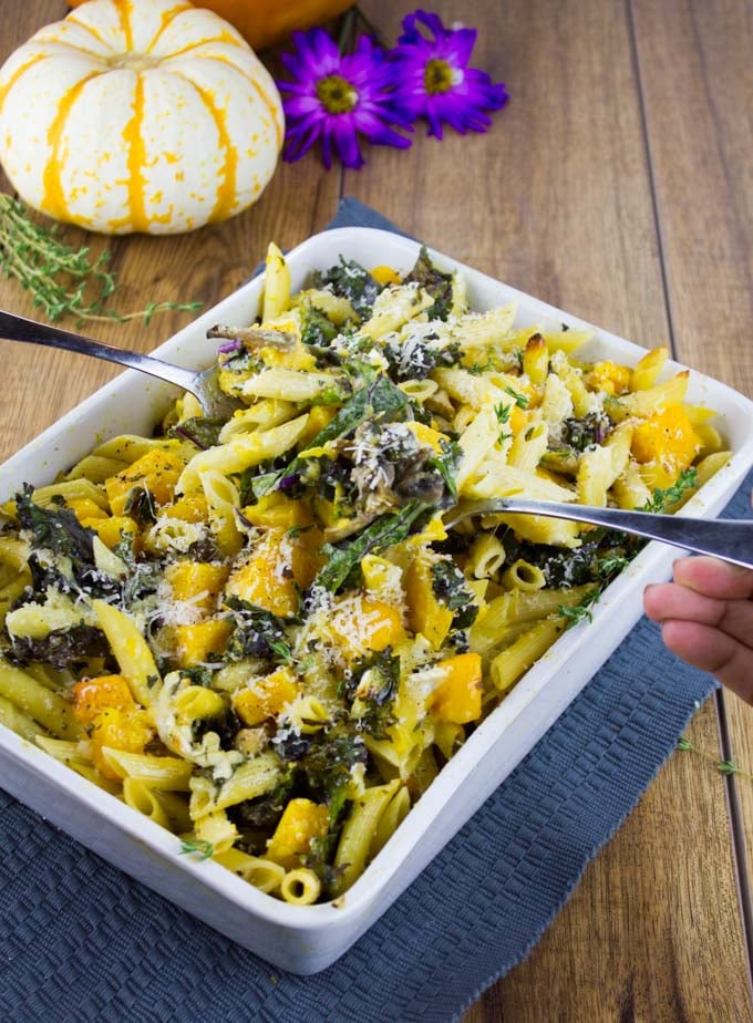  Easy Baked Pasta with Roasted Pumpkin, Kale and Mushrooms in a casserole on a blue place mat with a pumpkin in the background