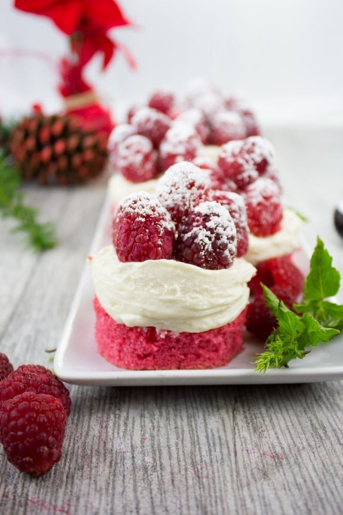 Mini Red Velvet Cheesecakes topped with sugar-dusted raspberries on a white plate