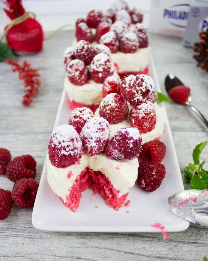 Mini Red Velvet Cheesecakes With Sugar-Dusted Raspberries on a white plate with raspberries on the side