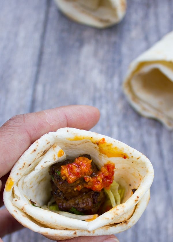 hand holding a pita cone filled with seared lamb shoulder and harissa sauce.