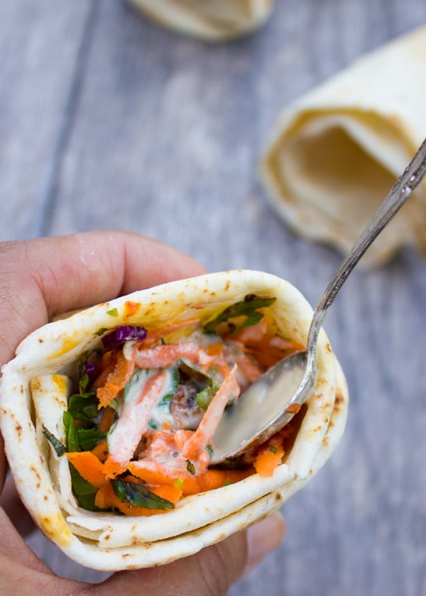 hand holding a pita cone filled with shredded carrot and drizzled with tahini sauce.