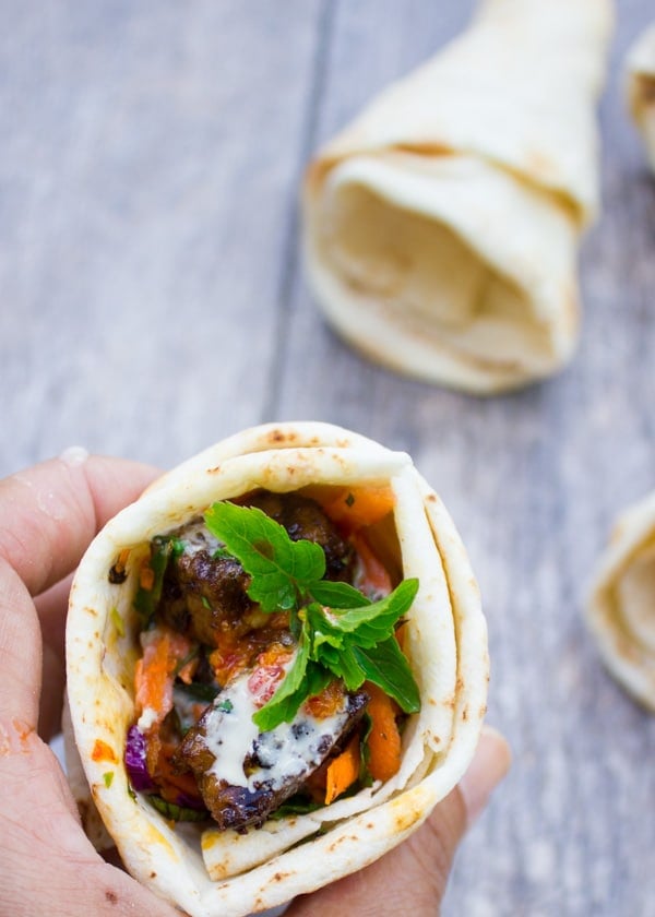 hand holding a pita cone filled with charred harissa lamb shoulder and shredded carrots.