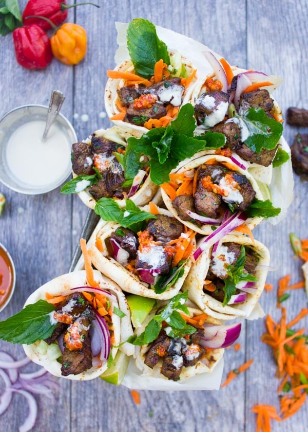 pita cones filled with grilled harissa lamb shoulder, grated carrots, lettuce and drizzled with Tahini sauce served in rectangular metal pan on a rustic wood table.